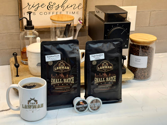 Bourbon Pecan and Maple Bourbon medium roast flavored coffees from The Lawman Coffee Co., with ground coffee bags, K-Cups, and a coffee mug in a Maryville, Tennessee kitchen.